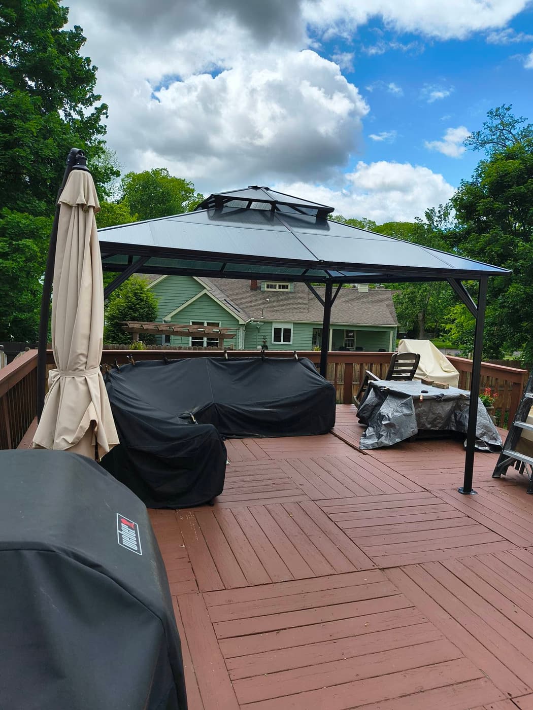 A gazebo set on a stained wood deck with a covered grill and patio furniture